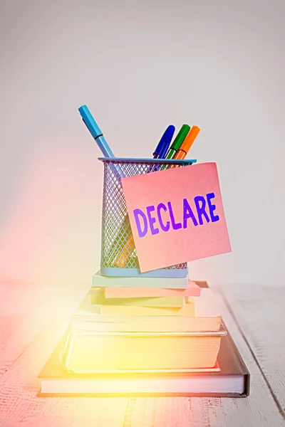 Handwriting text Declare. Concept meaning make known or state clearly especially in explicit or formal terms Stacked books pens metal holder sticky note lying vintage old wooden table.