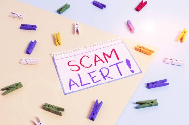 Scam Alert 'i gösteren not yazılıyor. İş fotoğraflarında sahtecilik yaparak kurbandan para kazanılıyor. Onu sarı mavi arka planlı renkli çamaşır iğnesi kâğıdı hatırlatıcısıyla ikna ederek..