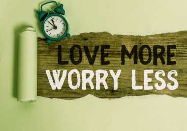 Kavramsal el yazısı Love More Worry less 'ı gösteriyor. İş fotoğrafı metni iyi bir davranış motivasyonuna sahip ol. Sevimli ol. Alarm saati ve yırtık kartonu ahşap masa arkaplanına koy..