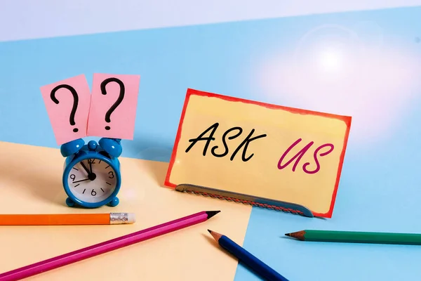 Handwriting text Ask Us. Concept meaning accepting questions or inquiry from showing Will answers any doubts Mini size alarm clock beside stationary placed tilted on pastel backdrop.