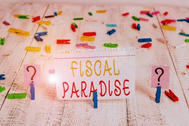 Word writing text Fiscal Paradise. Business concept for Tax on development Rates of taxation for foreign investors Scribbled and crumbling sheet with paper clips placed on the wooden table. clipart