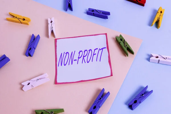 Word writing text Non Profit. Business concept for not making or conducted primarily to make profit organization Colored clothespin paper empty reminder yellow blue floor background office.