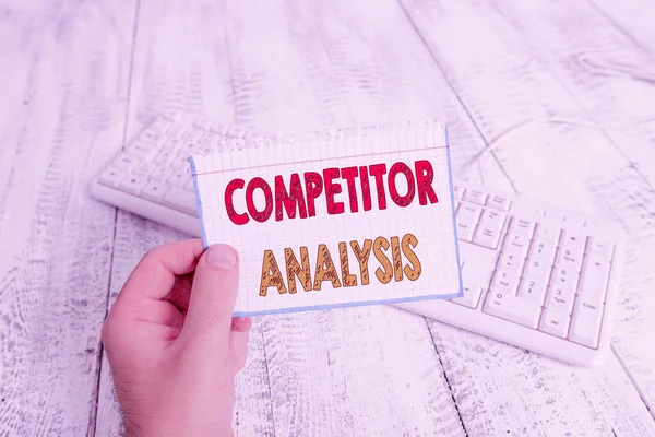 Text sign showing Competitor Analysis. Conceptual photo Determine the Strength Weakness of Competitive Market man holding colorful reminder square shaped paper white keyboard wood floor.