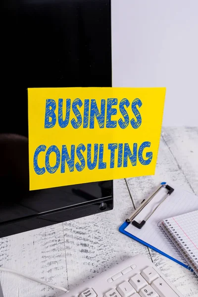 Письменный почерк Business Consulting. Понятие, означающее сочетание практики академической теоретической экспертизы Примечание к документу, приклеенному к черному компьютерному экрану рядом с клавиатурой и стационарным . — стоковое фото