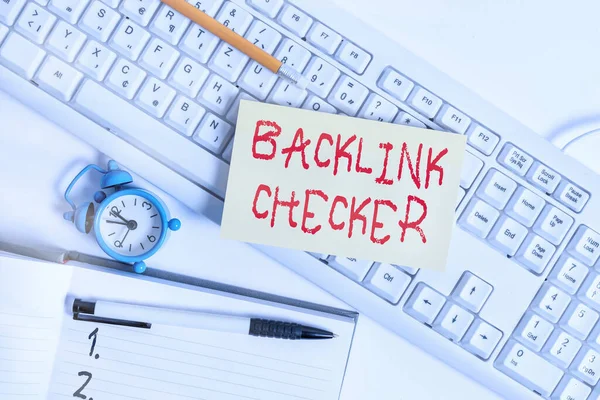 Signo de texto que muestra Backlink Checker. Foto conceptual Encuentra a tus competidores más valiosos y patrones planos colocados sobre papel de nota vacío en los lápices del teclado de la PC y el reloj . —  Fotos de Stock