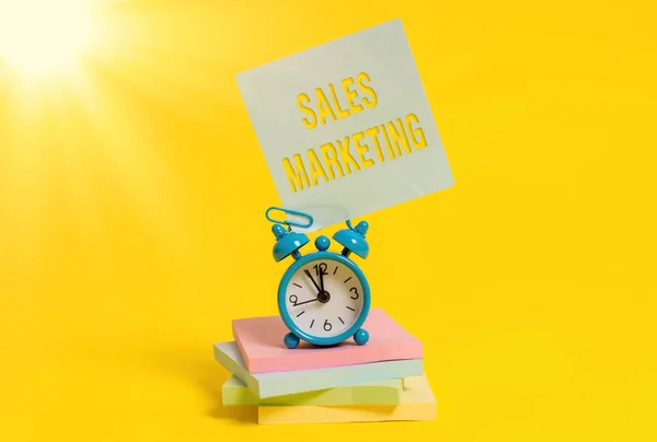 Word writing text Sales Marketing. Business concept for introducing product or service in order to get bought Metal alarm clock blank sticky note stacked notepads colored background.