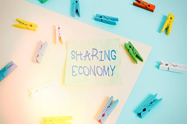 Writing note showing Sharing Economy. Business photo showcasing economic model based on providing access to goods Colored clothespin paper reminder with yellow blue background.