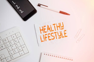 Sağlıklı Yaşam Tarzını gösteren bir not yazıyorum. İş fotoğraflarının gösterildiği, fiziksel aktivite ve egzersiz için canlı yayın cep telefonu kaleminin üzerinde yatar ve not kağıdını kopyalardı..