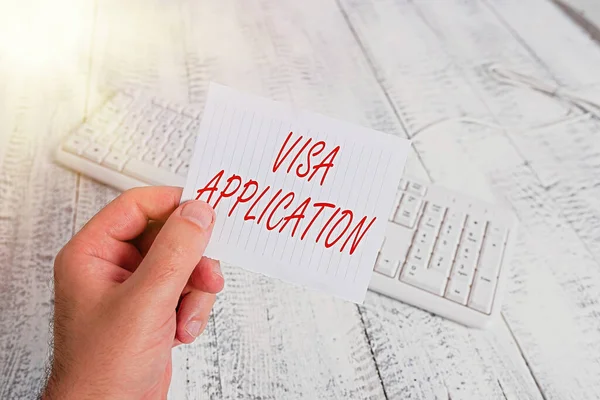 Word writing text Visa Application. Business concept for Form to ask permission travel or live in another country man holding colorful reminder square shaped paper white keyboard wood floor.