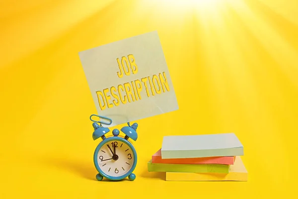 Handwriting text writing Job Description. Concept meaning A document that describes the responsibilities of a position Metal alarm clock blank sticky note stacked notepads colored background.