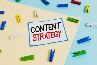 İçerik Stratejisini gösteren kavramsal el yazısı. İş fotoğrafı metni iyi fotoğraflar ve kelimeler kullanarak pazarlama planı oluşturur. Sarı mavi arkaplan ile renkli çamaşır iğnesi kağıt hatırlatıcısı.