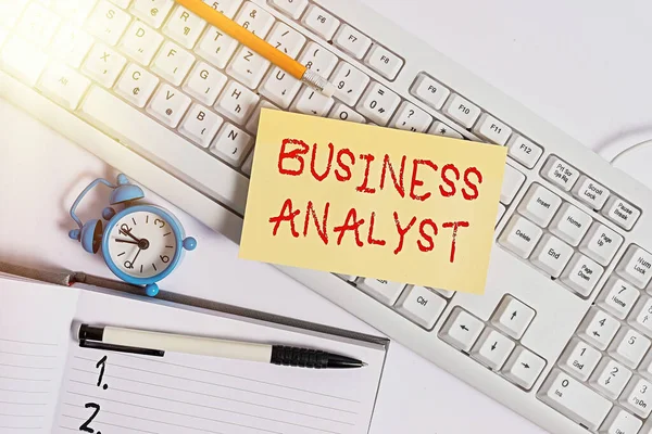 Text sign showing Business Analyst. Conceptual photo someone who analyzes big organization or website domain Flat lay above empty note paper on the pc keyboard pencils and clock.