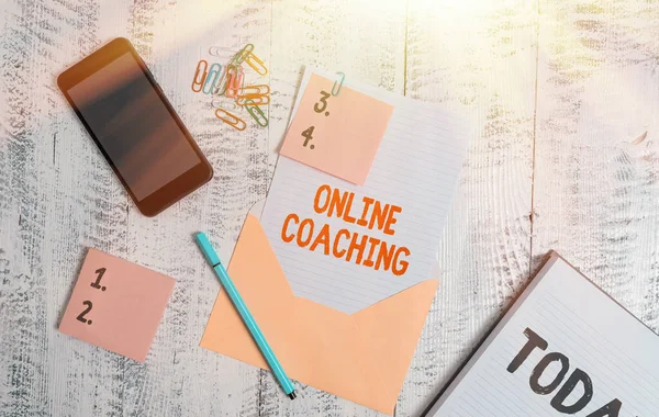 Handwriting text Online Coaching. Concept meaning Learning from online and internet with the help of a coach Envelope sheet smartphone sticky notes pen notepad clips wooden background.