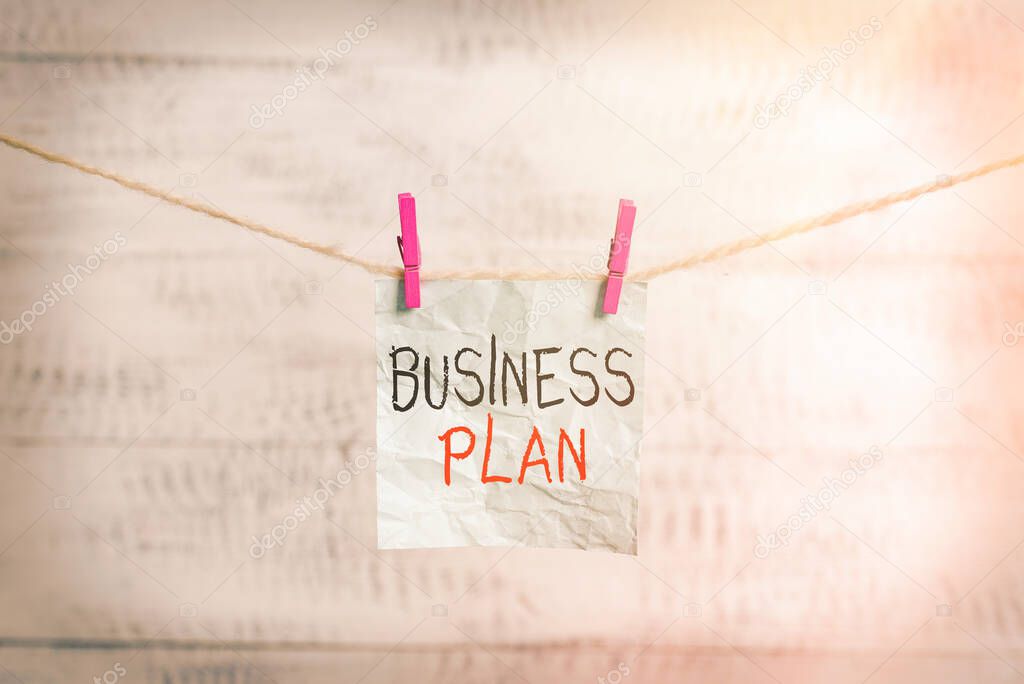 Writing note showing Business Plan. Business photo showcasing Structural Strategy Goals and Objectives Financial Projections Clothesline clothespin rectangle shaped paper reminder white wood desk.
