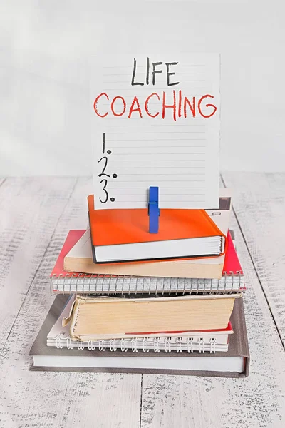 Woord schrijven tekst Life Coaching. Business concept voor het verbeteren van levens door uitdagingen moedigt ons in onze Carrières stapel gestapelde boeken notebook pin wasknijper gekleurde herinnering wit hout. — Stockfoto