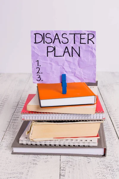 Handwriting text Disaster Plan. Concept meaning Respond to Emergency Preparedness Survival and First Aid Kit pile stacked books notebook pin clothespin colored reminder white wooden. — Stock Photo, Image