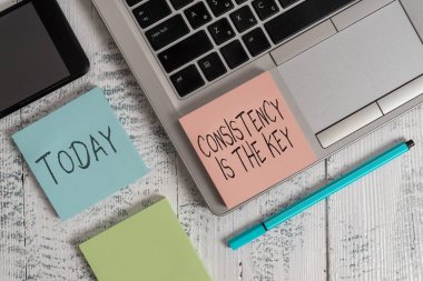 El yazısı tutarlılığı anahtardır. Kötü alışkanlıklardan kurtulma ve iyi alışkanlıklar oluşturma kavramı Metalik dizüstü bilgisayar yapışkan not defterleri eski ahşap masa yatağında duran kalem akıllı telefon..