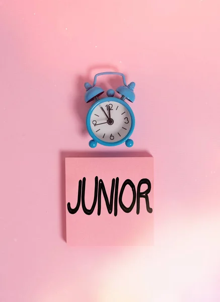 手書きテキスト執筆ジュニア.コンセプトは、他の誰よりも若い年の特定の数である人を意味しますヴィンテージ目覚まし時計のウェイクアップブランクノートパッド付箋色の背景. — ストック写真