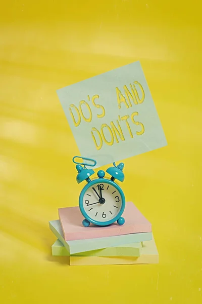 El yazısıyla "Do S and Don 't TS". Bazı eylemler veya eylemlerle ilgili kurallar veya gelenekler anlamına gelen kavram Metal alarm saati boş yapışkan not defteri renkli arkaplan. — Stok fotoğraf