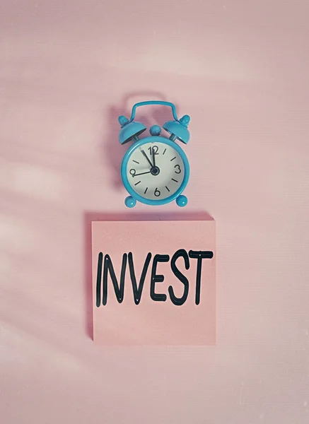 手書きのテキスト書き込み｜Invest。利益を達成することを期待して、商業ベンチャーを意味する概念ヴィンテージ目覚まし時計のウェイクアップブランクノートパッド付箋色の背景. — ストック写真