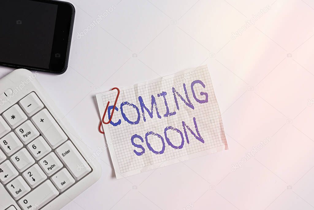Handwriting text Coming Soon. Concept meaning event or action that will happen after really short time White pc keyboard with empty note paper above white background and mobile phone.