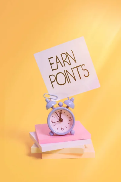 Handwriting text Earn Points. Concept meaning getting praise or approval for something you have done Metal alarm clock blank sticky note stacked notepads colored background.