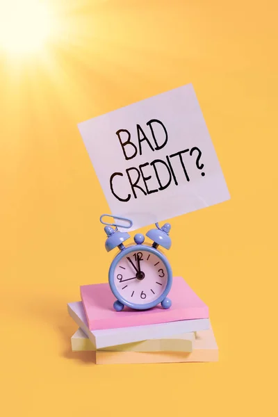 Handwriting text Bad Creditquestion. Concept meaning inabilityof an individual to repay a debt on time and in full Metal alarm clock blank sticky note stacked notepads colored background.
