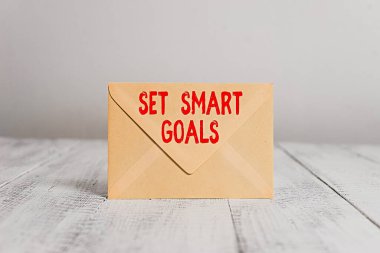 El yazısı yazıları Akıllı Hedefler Ayarla. Kavram, hedeflerin belirlenmesinde rehberlik etmek anlamına gelir. Kapalı dikdörtgen renkli zarf, eski ahşap vintage arka plan..