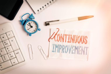 Devamlı gelişmeyi gösteren kavramsal el yazısı. Ürün ve süreçleri geliştirmek için sürdürülen iş fotoğrafı metni bilgisayar cep telefonu saati kalem ve not kağıdının üzerinde yatıyordu.