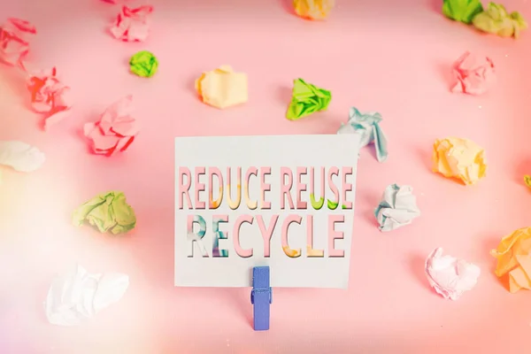 Word writing text Reduce Reuse Recycle. Business concept for environmentallyresponsible consumer behavior Colored crumpled papers empty reminder pink floor background clothespin.