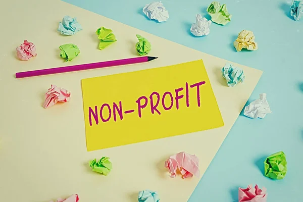 Handwriting text Non Profit. Concept meaning type of organization that does not earn profits for its owners Colored crumpled papers empty reminder blue yellow background clothespin.