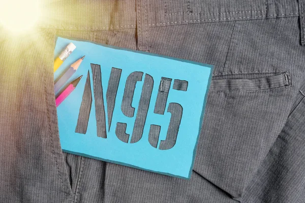 N95 'i gösteren kavramsal el yazısı. İş fotoğraflarında, giyeni korumak için kullanılan bireysel koruyucu ekipmanlar ve pantolon cebinde mavi not kağıdı sergileniyor..