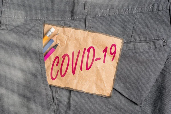 Teks tulisan tangan Covid19. Konsep makna penyakit pernapasan ringan hingga berat yang disebabkan oleh alat tulis coronavirus dan kertas catatan coklat di dalam saku celana kerja manusia. — Stok Foto