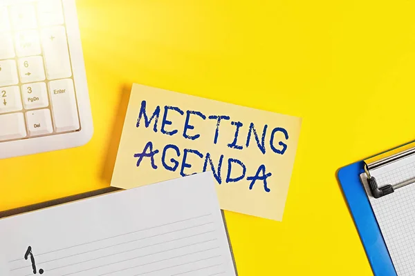 Writing note showing Meeting Agenda. Business photo showcasing items that participants hope to accomplish at a meeting Empty orange paper with copy space on the yellow table.