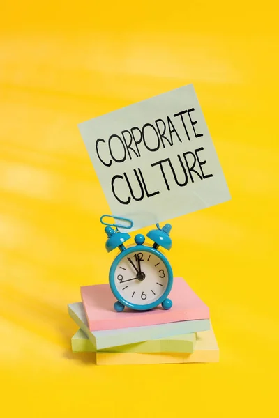 Handwriting text Corporate Culture. Concept meaning pervasive values and attitudes that characterize a company Metal alarm clock blank sticky note stacked notepads colored background.