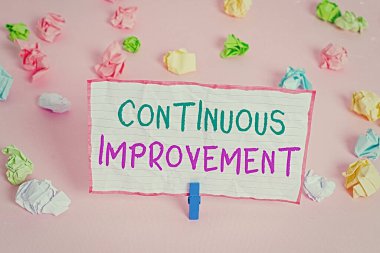 Metin işareti sürekli gelişim gösteriyor. Ürün ve süreçleri geliştirmek için kavramsal fotoğraf devam eden çaba Renkli buruşuk kağıtlar boş hatırlatıcı pembe zemin çamaşır mandalı.