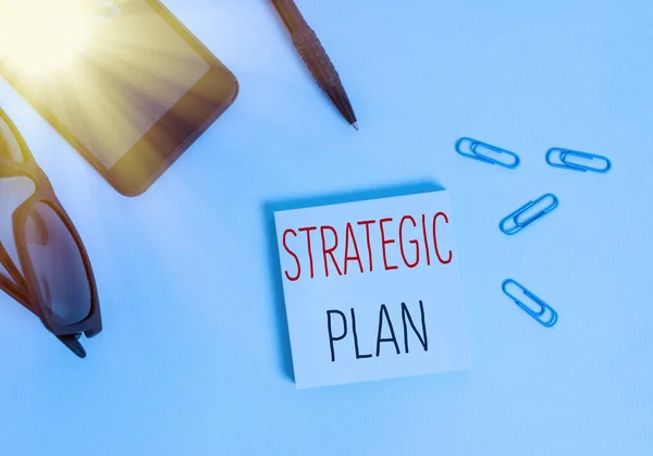 Text sign showing Strategic Plan. Conceptual photo a systematic process of envisioning a desired future Eyeglasses colored sticky note smartphone cell clips pen pastel background.