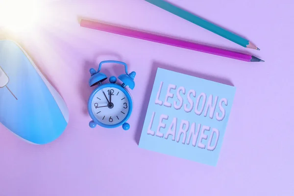 Text sign showing Lessons Learned. Conceptual photo the knowledge or understanding gained by experience Alarm clock wakeup blank notepad mouse markers colored background. — Stock Photo, Image