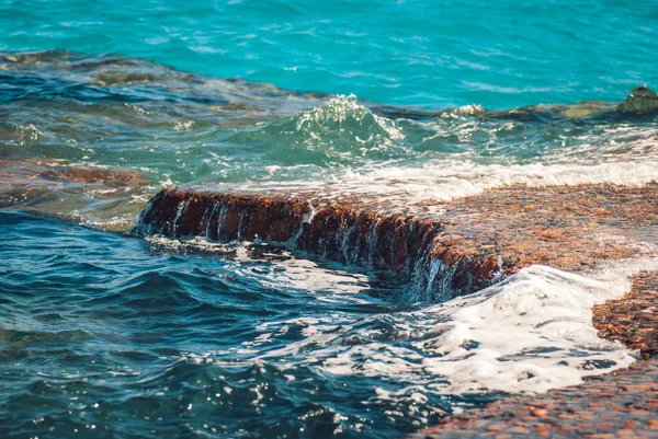 石の風景の背景に波紋と明るいスプラッシュと美しいクリアターコイズブルーの海の水の表面の写真、水平方向の画像 — ストック写真