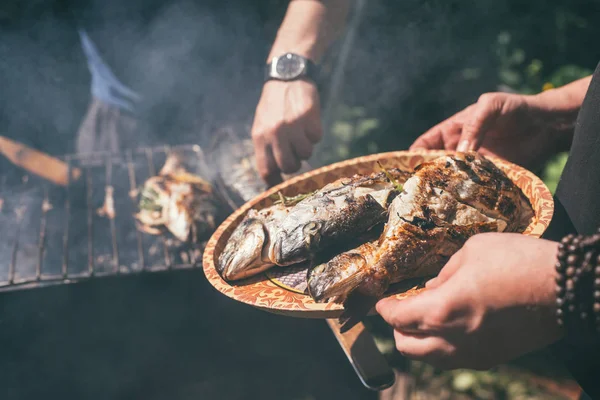 Muž drží talíř s hotovým jídlem. vynikající a čerstvé grilované ryby s citronem na grilu grilu v zahradě v létě. Selektivní zaostření makra s mělkým Dof — Stock fotografie