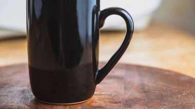 Ahşap yuvarlak bir masanın üzerinde duran, arka planı bulanık siyah, parlak bir fincan.