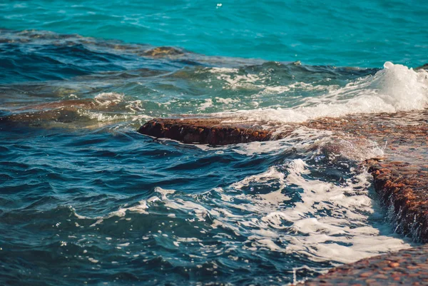 石の風景の背景に波紋と明るいスプラッシュと美しいクリアターコイズブルーの海の水の表面の写真、水平方向の画像 — ストック写真