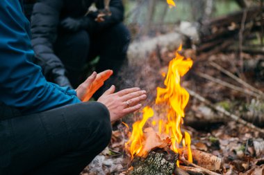 Adam ellerini ateşte ısıtıyor. Akşamları ormanda odun yakmak. Doğadaki turistik kampta kamp ateşi. Barbekü ve açık havada temiz hava. Ateş ve alev soyut karanlık arkaplanda kıvılcımlar saçar