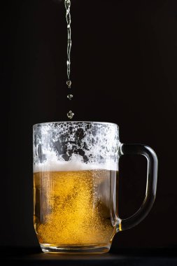 Parlak ve taze biralar büyük bir cam kadehe dökülüyor. Siyah arkaplanda izole edilmiş sığ alan derinliğiyle seçici odak makro görüntüsü