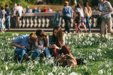Moskova, Rusya-09 Mayıs 2015: Gorky Park 'ta insanlar Zafer Günü' nü kutluyor. St. George kurdeleli 3 genç kız nergislerin bahçesinde oturuyor ve arka planda fotoğraf çekiyor.