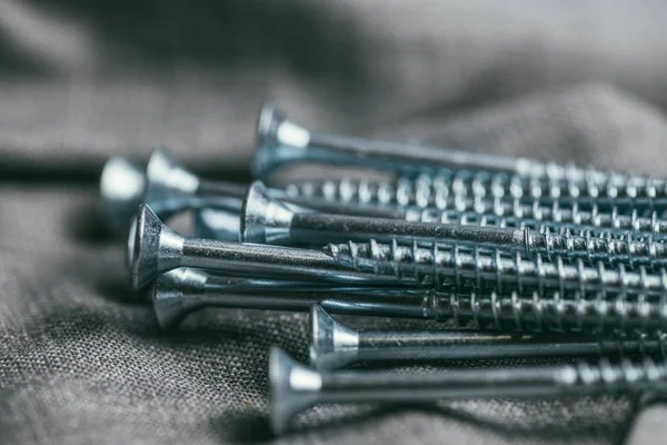 Un puñado de tornillos metálicos auto-cortadores se encuentra en el telón de fondo de una vieja tela de mezclilla. macro de enfoque selectivo con DOF poco profundo —  Fotos de Stock