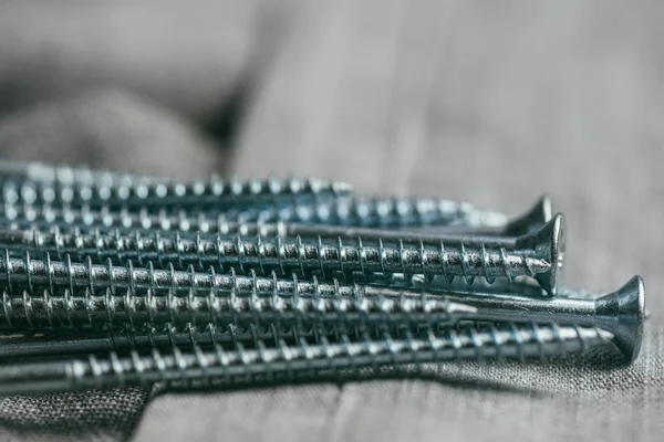 Un puñado de tornillos metálicos auto-cortadores se encuentra en el telón de fondo de una vieja tela de mezclilla. macro de enfoque selectivo con DOF poco profundo —  Fotos de Stock