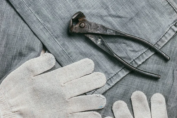 Luvas de trabalho de malha de segurança para uso industrial e alicates muito envelhecidos e enferrujados no fundo da ganga velha, áspera e enrugada. Vista superior de Flatlay — Fotografia de Stock