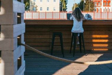 İş adamı, orta boylu, beyaz elbiseli bir kadın. Yoğun bir caddedeki bir kafede yüksek bar taburesinde oturuyor ve 5 gramlık internet bağlantısı kullanarak bir dizüstü bilgisayar üzerinde çalışıyor.