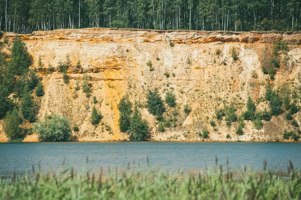 Alta orilla empinada arenosa rocosa cubierta de pinos sobre un lago claro y azul — Foto de Stock